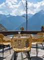 yellow chairs, round table, wooden railing, potted plants, mountain view