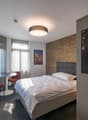 A bedroom with a single bed, bedside tables, a TV, a painting on the wall, and two red chairs next to a round table.