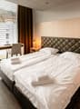 Spacious bedroom with large windows, quilted headboard, bedside tables, and a desk area