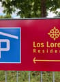 Red sign with blue and white parking symbol, text 'Los Lorentes Residences', arrow pointing right