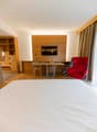 A bedroom with a large bed, a desk, a TV, and a chair.