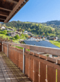 Wooden balcony with a scenic view of a mountainous village with houses, trees, and a clear blue sky.