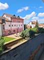 Building with multiple floors, red roof, balcony, concrete wall, plants, street light, houses in the background
