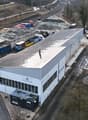 Industrial building with several trucks parked, storage area with containers and a small building.