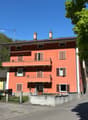 3-story apartment building with a red exterior, balconies on each floor, and chimneys on the roof.