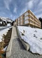 Modern wooden and stone building, multiple balconies, multiple levels, snow-covered hill