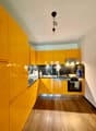 modern kitchen with yellow cabinets, wooden floor, stainless steel appliances, black countertops