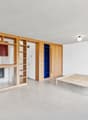 Open-concept studio apartment with wooden shelving units, a kitchenette with a dishwasher, and a raised platform bed area