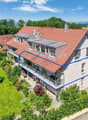 3-story house with red tile roof, white exterior, multiple balconies, surrounded by lush greenery and trees, with a trampoline in the yard