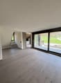 Spacious open-plan living area with large windows overlooking a balcony or terrace, hardwood flooring, and a staircase leading to another level.