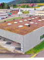 Large commercial building with a green roof, surrounded by parking spaces and other industrial buildings. The building has a modern, industrial design with a flat roof and large windows.