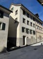 Concrete building with multiple windows and green shutters, street entrance, paved street.