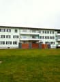 3 story apartment building, green exterior, multiple balconies, large grassy area in front
