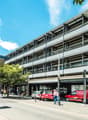 multi-story building, white exterior, multiple windows, cars parked in front, street with cars and pedestrians