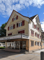 raised ground floor building, commercial use, multiple windows, slanted roof, red shutters, parking space