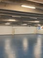 Empty room with blue floor, white walls, two doors, small windows, and ceiling lights