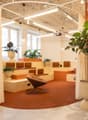 Open concept office space with exposed wooden ceiling, large windows, comfortable seating areas, potted plants, and modern lighting fixtures