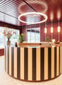 Spacious reception area with a circular wooden reception desk, decorative lighting fixtures, potted plants, and large windows providing natural light.