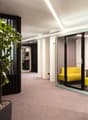 Modern office space with large potted plants, blue lockers, and a yellow sofa pod for private work or relaxation