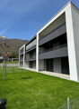 3-story modern apartment building with large windows, balconies, and a grassy lawn in front surrounded by a fence
