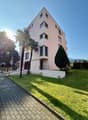 4 story apartment building, pink exterior, large windows, raised ground floor, palm trees, green lawn
