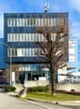 Modern office building with blue exterior, multiple windows, entrance with glass doors, street light, cars parked in front, bicycles parked, small tree in front, signboard with text 'safe' and 'ARMEDIZIN'.