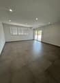 Spacious living room with large windows, gray tile flooring, and recessed lighting. The room has access to a balcony or terrace through sliding glass doors.