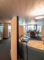 modern office space with glass walls, beige carpet, gray couches, wooden tables, and large windows