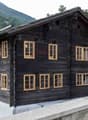 Traditional wooden chalet with yellow-framed windows, slate roof, chimney, mountain view