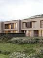 Modern architectural design, multiple windows, elevated ground floor, surrounded by a grassy area with a garden and a fence