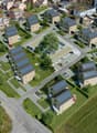 a housing development, featuring a variety of building styles and solar panels, including houses, parking garages, and green spaces with trees and grass