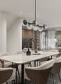 Spacious dining area with a large marble-top dining table and comfortable upholstered chairs. The room features a modern chandelier with glass globes, built-in shelving, and large windows overlooking a balcony or terrace area.