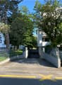 A parking lot with a garage entrance, surrounded by trees and a white building.