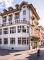 The building is a multistory white building with large windows. It has several floors and a lot of windows. The building looks modern and elegant with no visible exterior balconies. It has a balcony at the top floor. The building also features a triangula