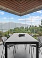 Spacious dining area with a large glass-enclosed patio, offering a panoramic view of the surrounding mountains and lush greenery. The room features a modern black dining table and chairs, with a wooden ceiling and beams providing a warm, rustic ambiance.