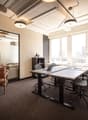 Empty office room with desks and chairs, large windows, potted plant, leather chair, small table