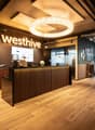 Wooden flooring, large chandelier, glass windows, wooden reception desk, couch, desk, large plant, sign