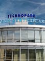 The image shows a large, modern building with a prominent sign that reads 'TECHNOPARK HIGHTECH-ZENTRUM AARGAU'. The building has a glass facade and appears to be a commercial or office space.