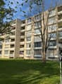 Multi-story apartment building with balconies, surrounded by trees and grass.