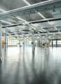 Empty warehouse with metal beams, exposed pipes, large windows, concrete floor.