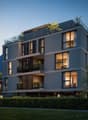 Modern multi-story building with glass balconies, illuminated windows, and a rooftop terrace with greenery.