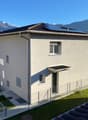 Modern 2 story house, solar panels on the roof, white exterior, fenced garden, mountains in the background