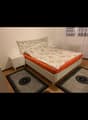 a bed with white headboard, white cabinet, and two rugs, white wall, window with curtains