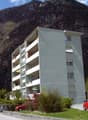 Multi-story building with multiple balconies, located at the base of a rocky mountain with steep slopes