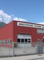 Red industrial building with large garage doors, multiple windows, and a sign reading 'MANUTENZIONE CISTERNE SA'.