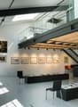 High ceiling, gallery-style space, glass railings, skylights, mounted pictures, furniture in a neat manner