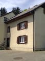 2 story house, beige walls, brown shutters, car parked in front, brick driveway