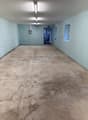 Empty room with light grey walls and concrete floor. There are fluorescent ceiling lights. There are small windows, one of which has a door.