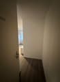 empty room, white walls, wooden floor, open door leading to bedroom, small white desk, white wardrobe, glass window with white curtain