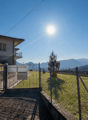 House with a balcony, surrounded by a fence, with a mailbox, a small garden, and a view of the mountains.